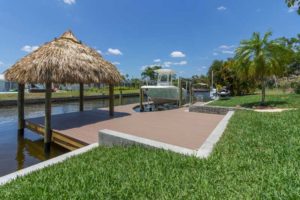 A boat dock with grass roof and palm trees.
