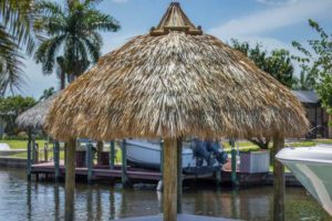 A boat dock with palm trees and a thatched roof.